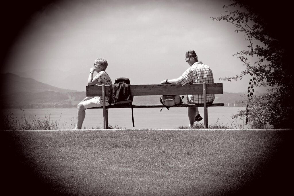 An older couple sitting on opposite sides of a bench.
