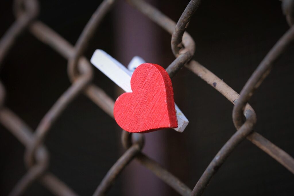 A clothes pin with a heart on it attached to a chain link fence.