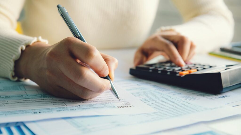 A woman filling out a 1040 form while using a calculator as she makes smart tax moves.