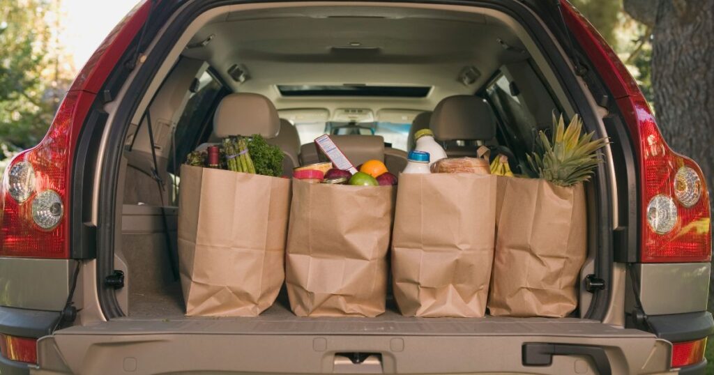 An open car rear hatch with 4 bags full of groceries. Affordability crisis